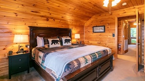 A wooden-paneled bedroom with a large bed, two bedside lamps, and a framed welcome sign. - Heavens Hideaway - 4 bedroom with views, allows pets, game tables (Lenoir)