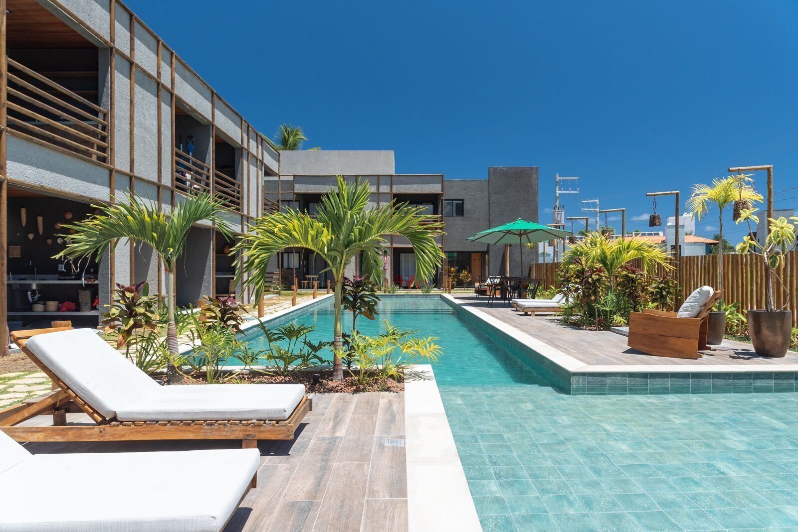 Ein moderner Poolbereich mit Liegestühlen, einem Pool und einem Gebäude mit großen Fenstern und einem Balkon.