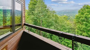 A balcony with a wooden railing overlooking a forested valley and distant mountains. - Modest condo with access to pool and hot tub B10 (Killington)
