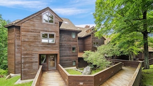 A modern wooden house with a sloped roof, a front porch, and a landscaped garden with a wooden deck. - 2-bedroom condo with pool and hot tub. (Killington)