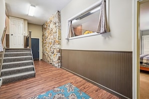 Un couloir doté d’un plancher en bois, d’un tapis à motifs, d’un mur en pierre et d’une fenêtre avec des rideaux.