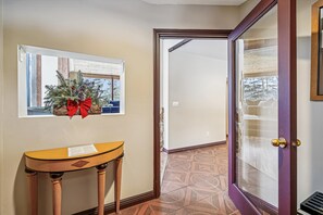 Un pasillo con una consola de madera, un cuadro enmarcado con un lazo rojo y una puerta que da a otra habitación.
