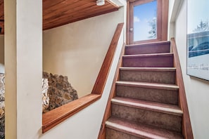 Un escalier avec des rampes en bois et des marches recouvertes de moquette, menant à une pièce dotée d’un mur en pierre et d’une fenêtre.