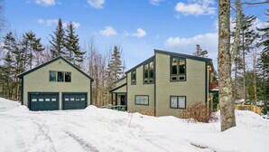 A two-story house with a garage, surrounded by snow-covered ground and trees. - 3 Bedroom Pet Friendly with Hot Tub Birch Beauty (Killington)