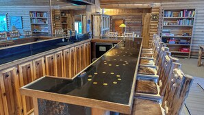 A wooden bar with a black countertop and stools. - Stanley House - Hillside Cabin with Panoramic Views of the Sawtooth Mountains (Stanley)