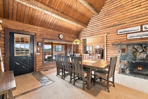 A log cabin interior with a dining area, a fireplace, and a view through the door.