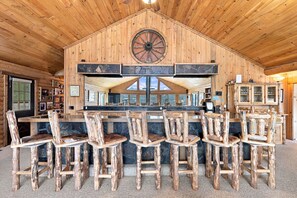 Un intérieur rustique en bois, avec un coin bar doté de chaises en bois et d’une cheminée en pierre.