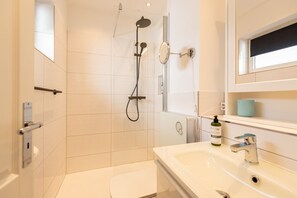 Een moderne badkamer met een douche, toilet, wastafel en een spiegel.