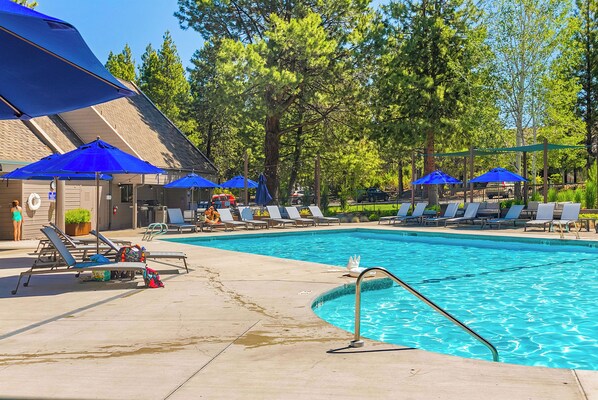 A swimming pool with blue umbrellas, lounge chairs, and a building with a sloped roof. - Alpine Studio at Mount Bachelor (Bend)