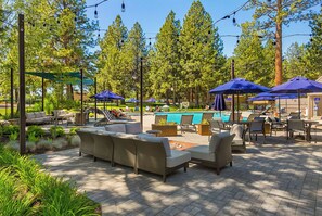 An outdoor patio area with wicker furniture, umbrellas, and a pool. - Alpine Studio at Mount Bachelor (Bend)