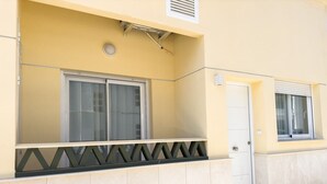 A building with a yellow facade, a white door, and a window with a metal grille.