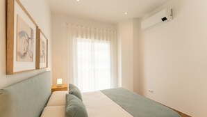 A bedroom with a bed, a nightstand, a window with curtains, and an air conditioning unit.