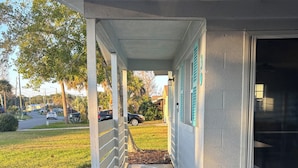 A covered porch with a concrete floor, a wicker sofa with cushions, and a view of a street with parked cars and greenery. - Entire Home: 4 Blocks to Ocean-Jacksonville Beach (Jacksonville Beach)