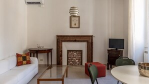 A living room with a fireplace, a sofa, a coffee table, a television, and a dining table. - Panisperna 193 - FromHometoRome (Roma)