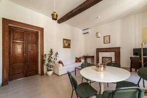 Un comedor con una mesa redonda, sillas verdes, un sofá blanco, una planta en maceta y una chimenea.