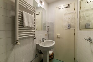 Un baño con un lavamanos blanco, un perchero, un espejo y una puerta con una toalla colgada.