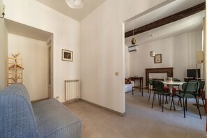 Een ruime woonkamer met een bank, een eettafel met stoelen, een open haard en een televisie.