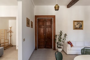 A hallway with a wooden door, a white sofa, a green chair, and a potted plant.