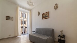 A living room with a grey sofa, a small black side table, and a door leading to a balcony. - Panisperna 193 - FromHometoRome (Roma)
