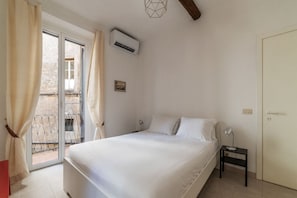 Een slaapkamer met een bed, nachtkastje, lamp, airconditioning en een deur.