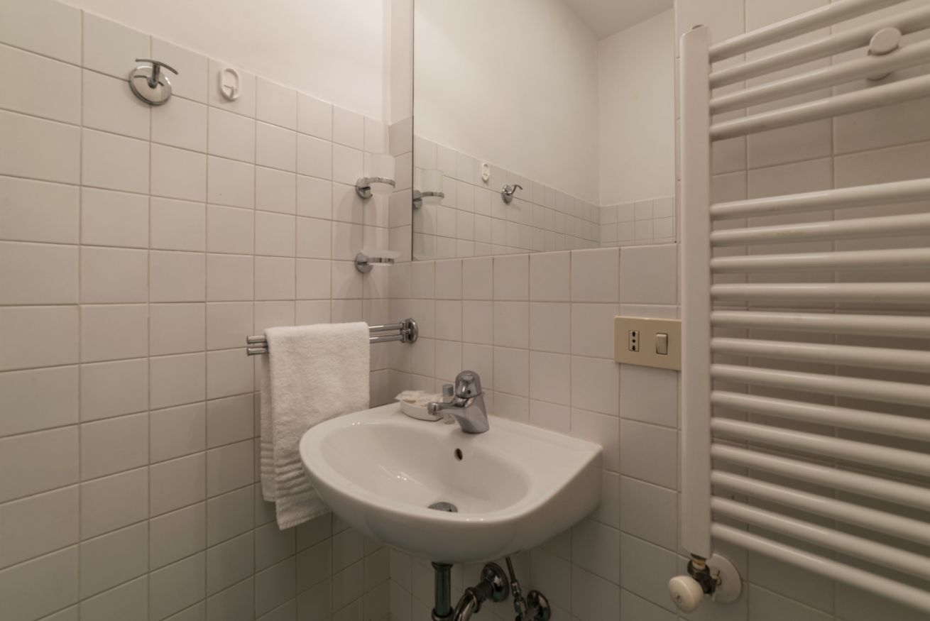 Een badkamer met witte tegels, een wastafel, een handdoek en een radiator.