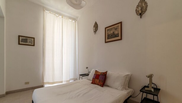 A bedroom with a large bed, a bedside table, a lamp, and a window with curtains. - Panisperna 193 - FromHometoRome (Roma)