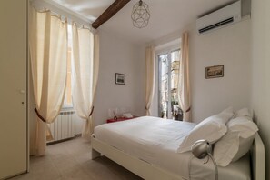 A bedroom with a bed, curtains, a radiator, a picture on the wall, and an air conditioning unit.