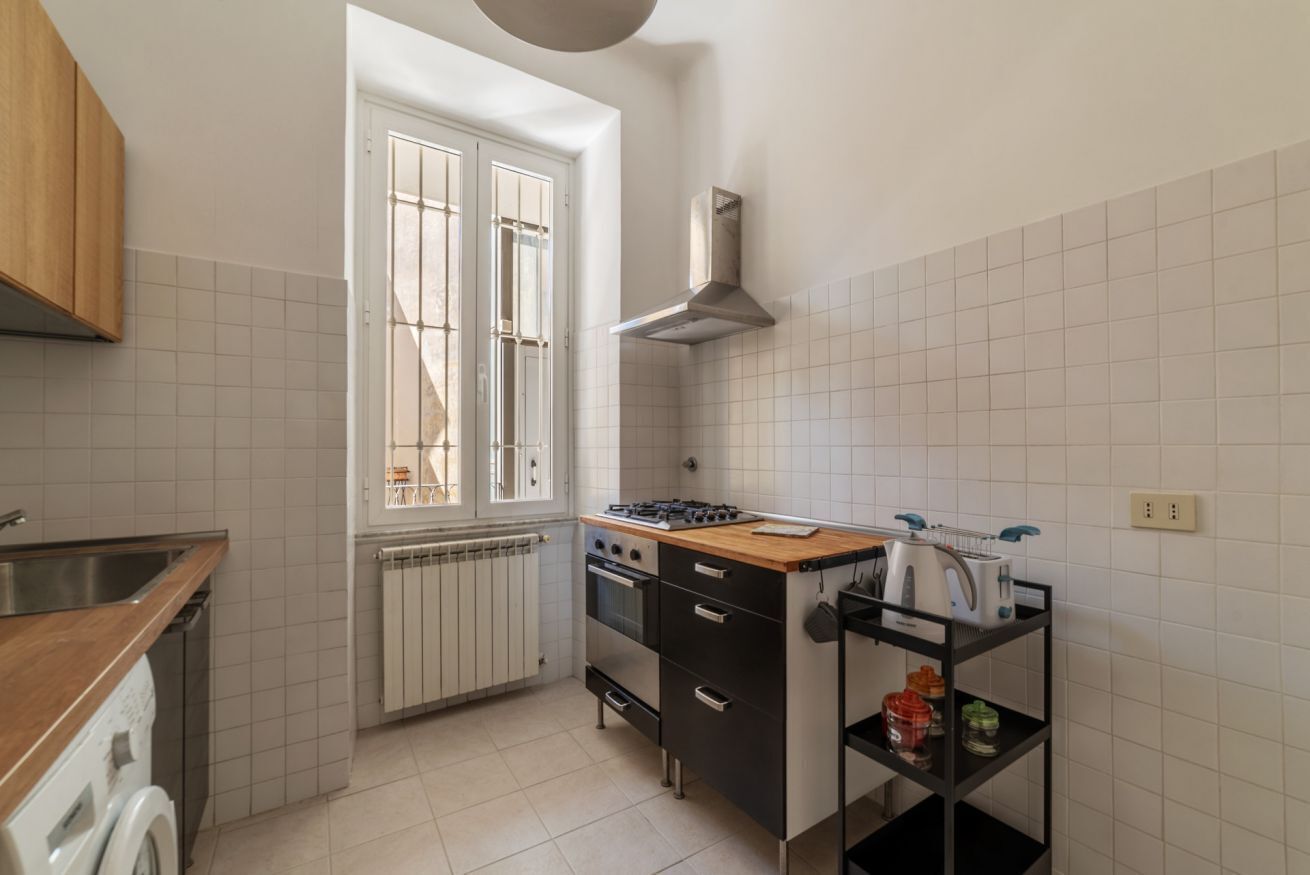 A compact kitchen with a stove, oven, and a small countertop. There is a window with a view of the outside, and a radiator under the window.