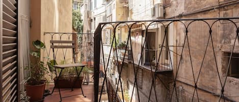 A narrow outdoor corridor with a metal gate, potted plants, and a small table.