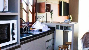 A compact kitchen with a built-in microwave, a sink, and a small bar area with stools. - Pousada Rota das Cachoeiras Urupema (Urupema)