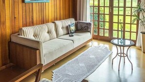 A wooden-paneled room with a sofa, a painting, a glass table, and a view through a large window. - Pousada Rota das Cachoeiras Urupema (Urupema)