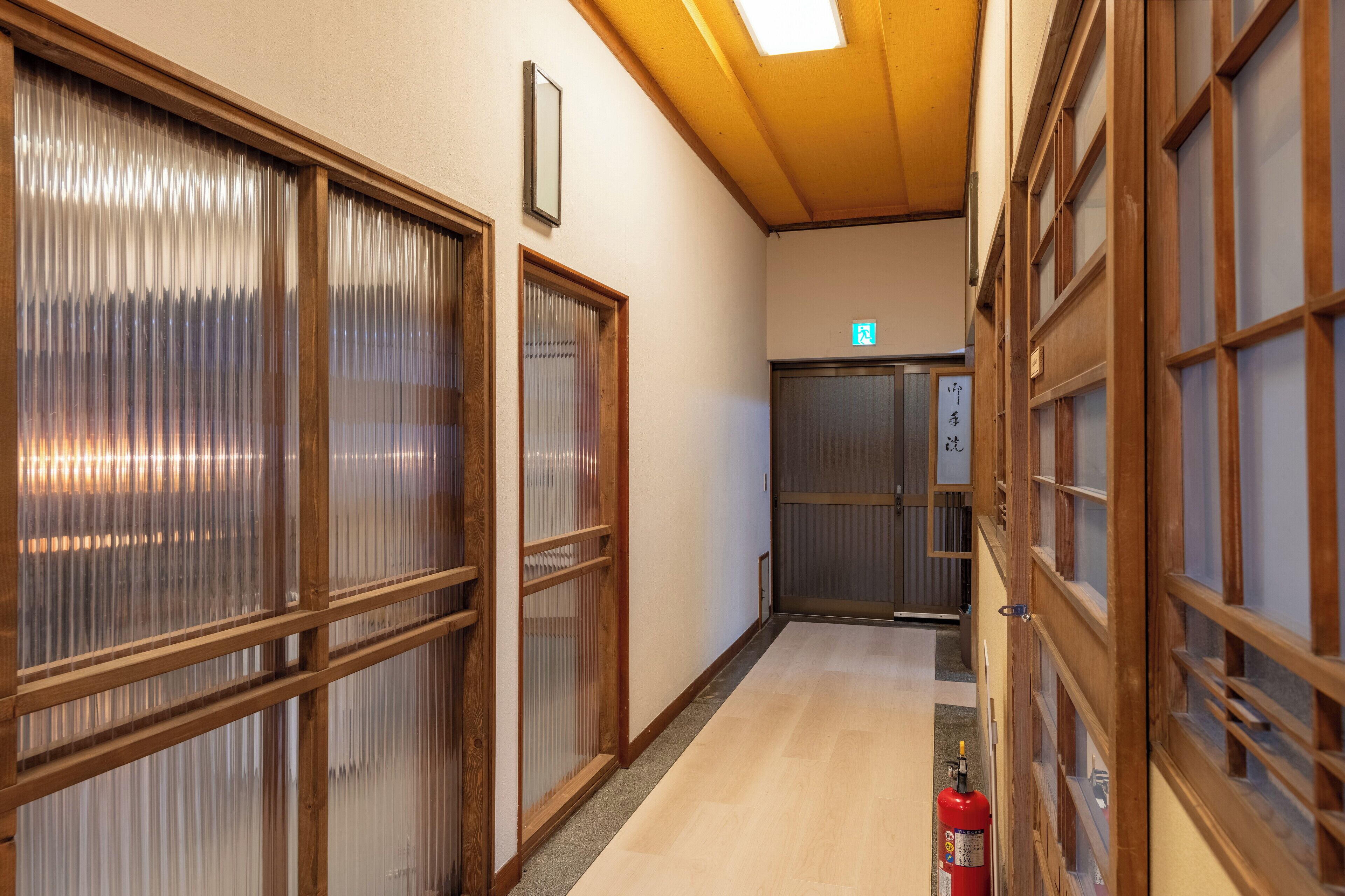 Un couloir doté de portes coulissantes en bois, d’un extincteur et d’un ascenseur.