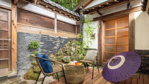 Un espace extérieur aménagé dans le style traditionnel japonais, avec des tatamis, un mur de pierre et une terrasse en bois.