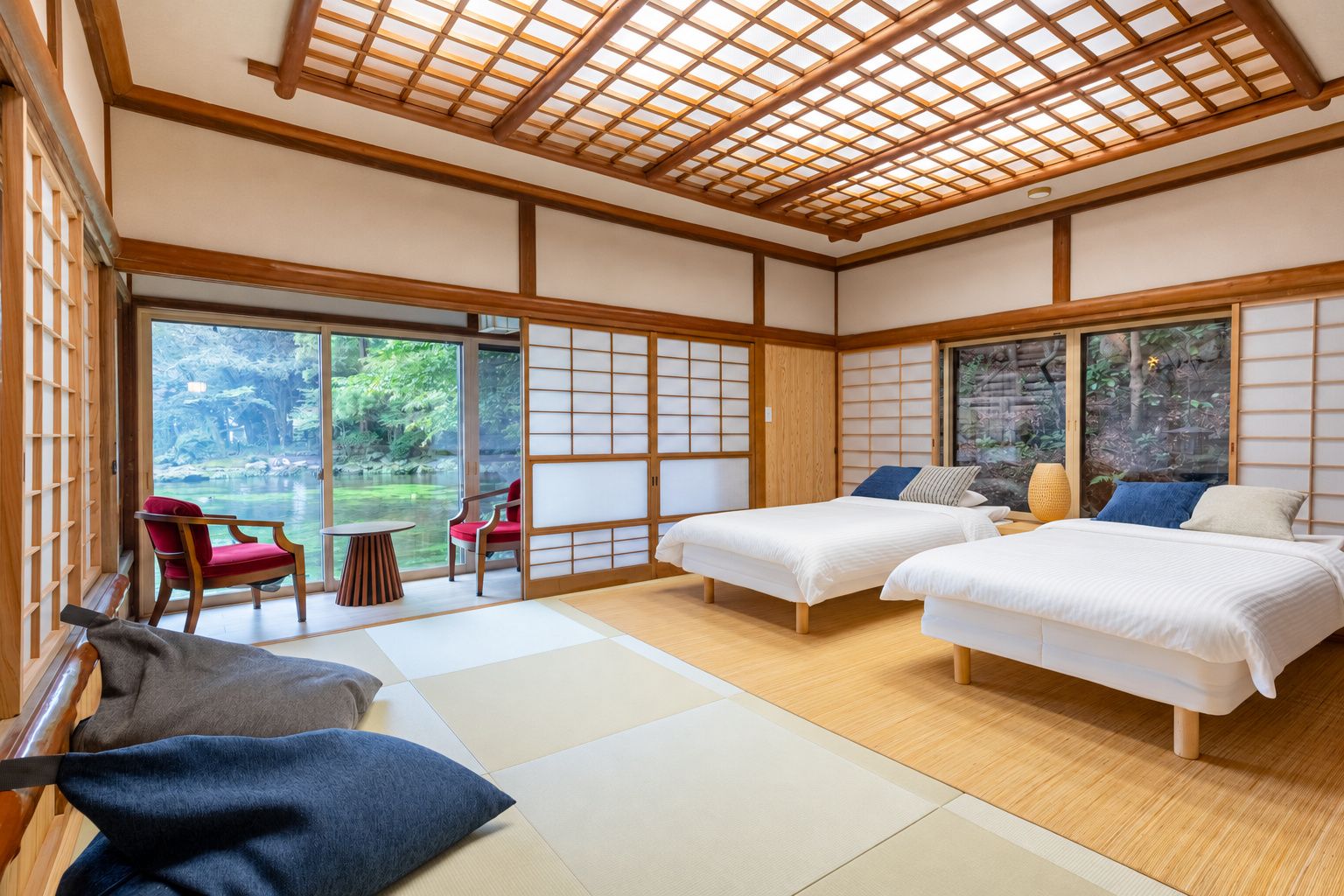 A traditional Japanese-style room with tatami flooring, two beds, a sliding door, and a view of a garden.