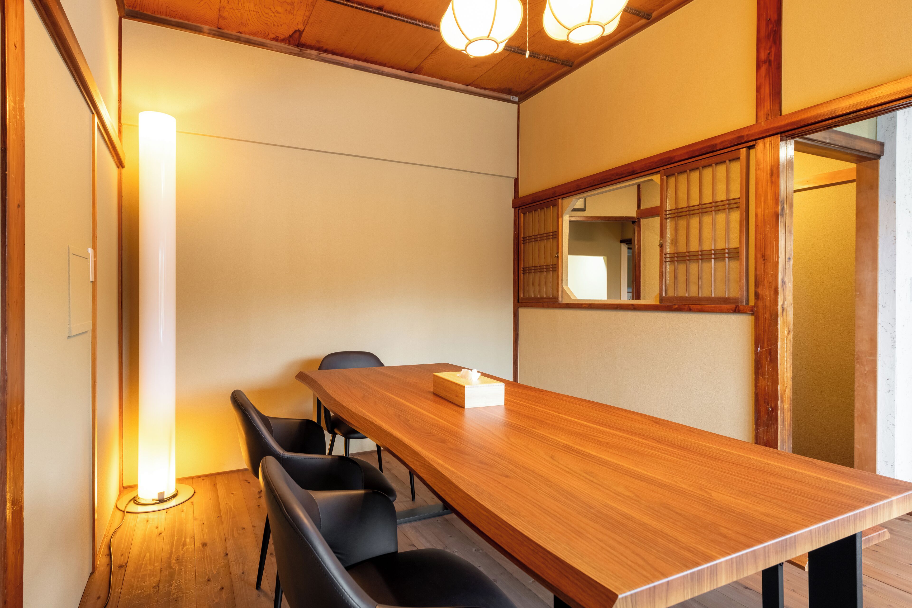 A conference room with a wooden table, black chairs, a standing lamp, and a traditional Japanese shoji screen.
