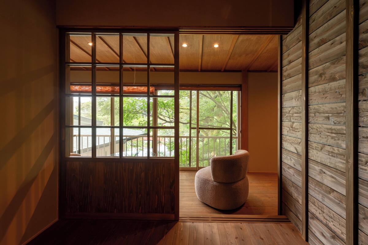 Una habitación con un ventanal grande, suelo de madera y un sillón acolchado.