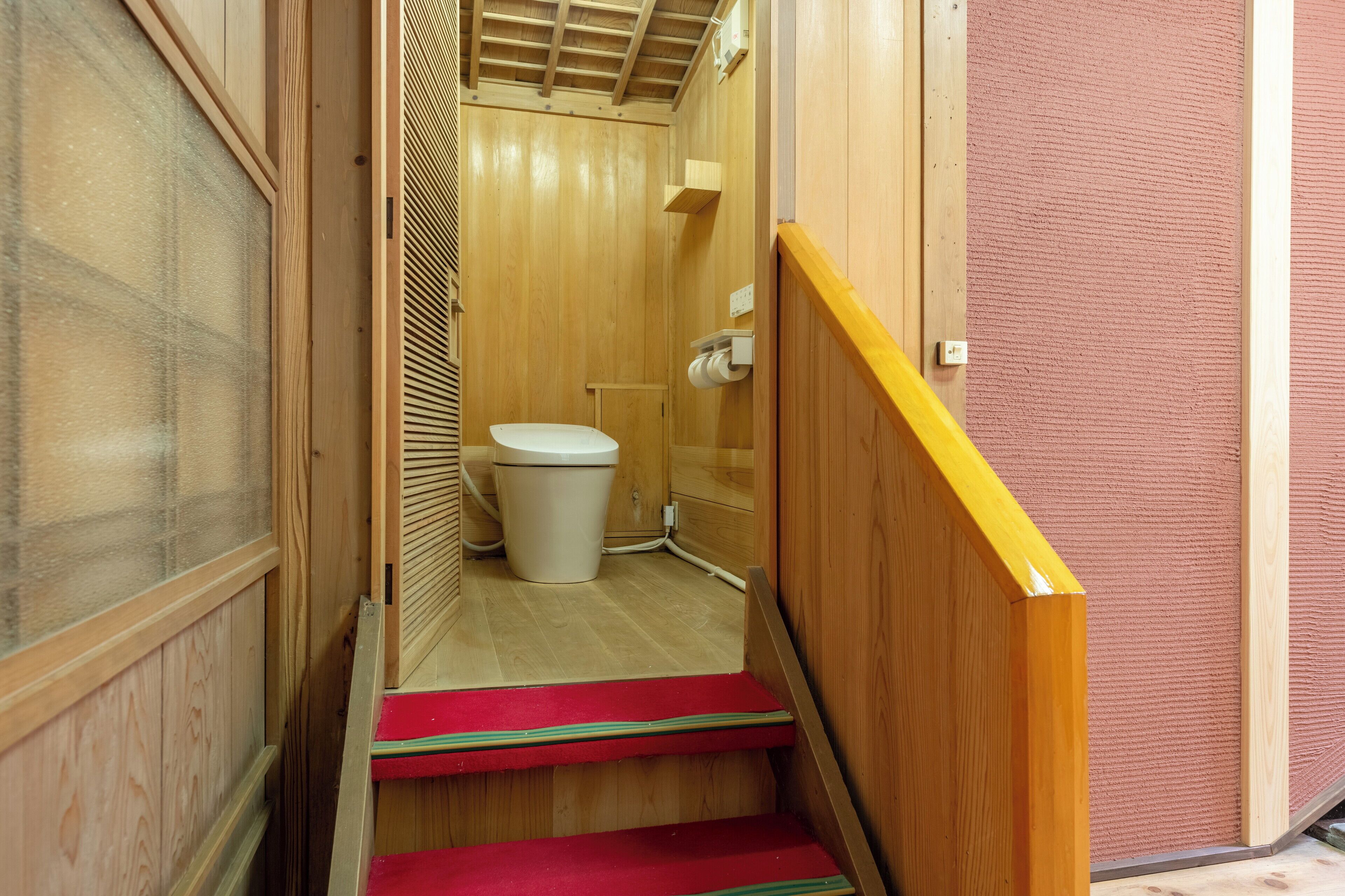 Een smalle houten trap die leidt naar een kleine badkamer met toilet en douche.