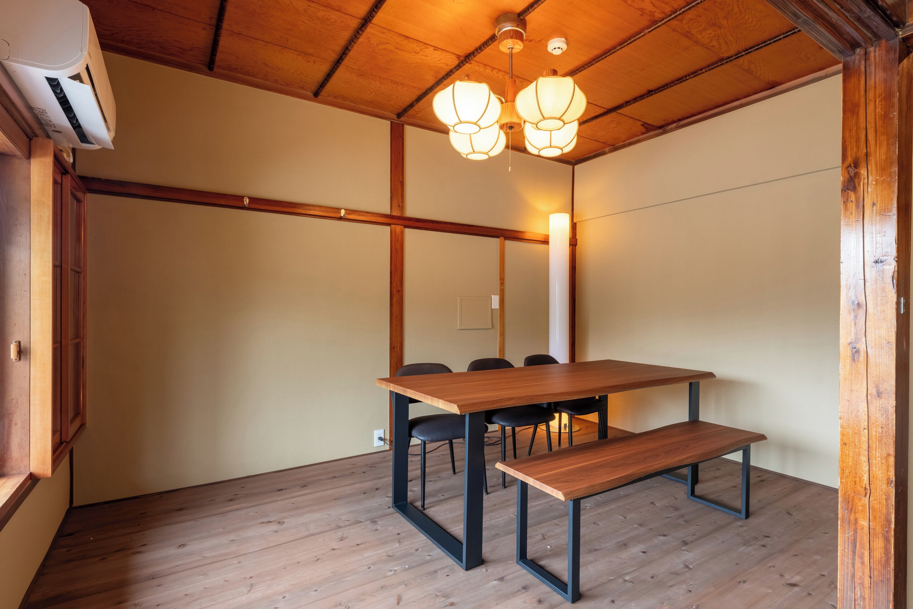 A room with a wooden table and benches, a ceiling with wooden beams, and two hanging light fixtures.