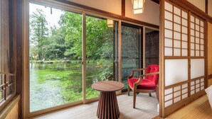 Une pièce dotée d’une grande porte-fenêtre coulissante donnant sur un étang, d’une table en bois et d’une chaise rouge.