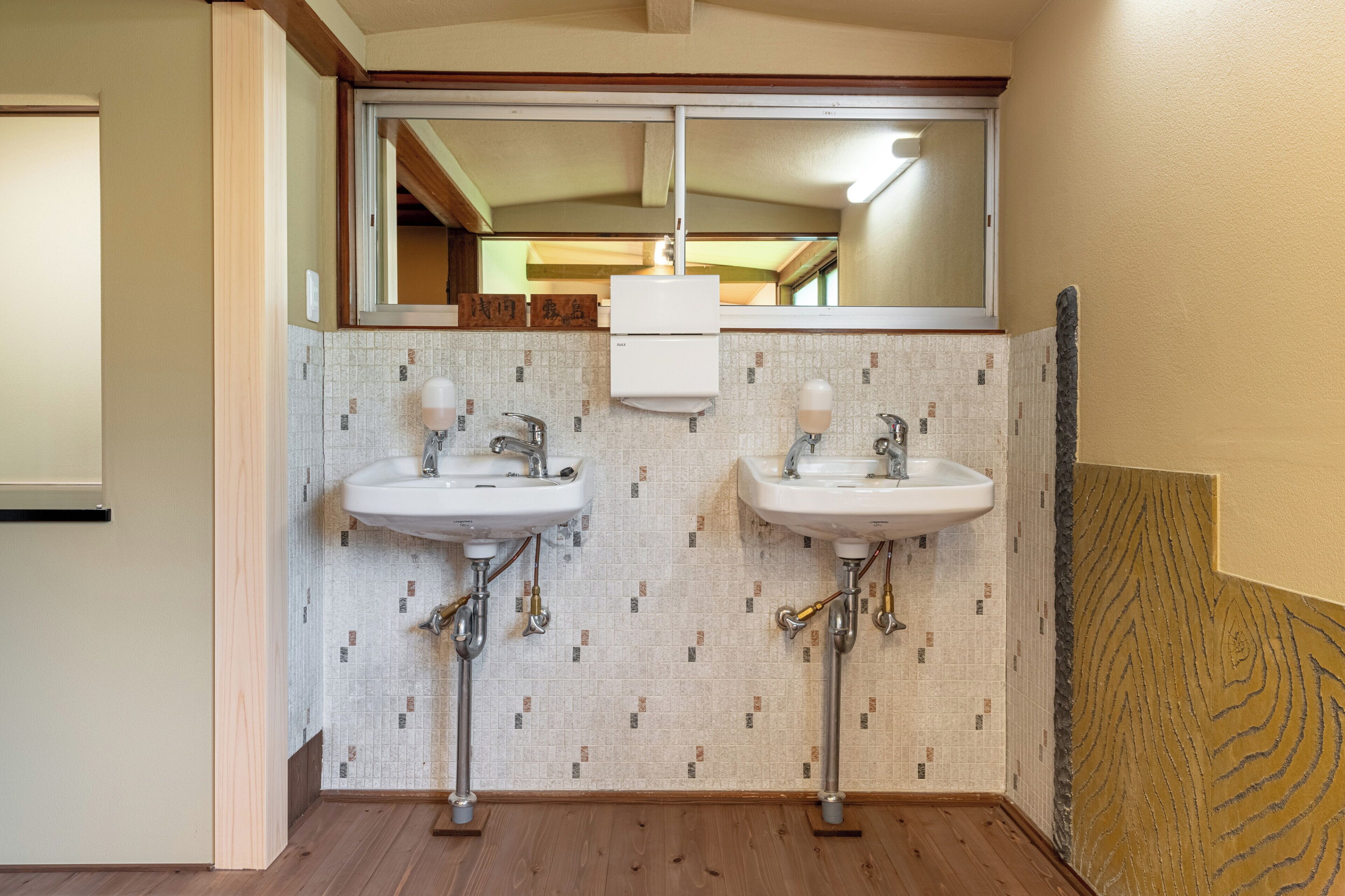 A bathroom with two sinks, a mirror, and a window above the sinks.