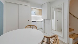 A compact kitchen with white cabinets, a dining area with a round table and wicker chairs, and a staircase leading to an upper level. - True Setúbal, Residence (Setúbal)