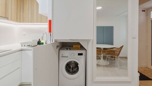 A compact kitchen with a built-in washer and dryer, a small countertop, and a dining area with wicker chairs. - True Setúbal, Residence (Setúbal)