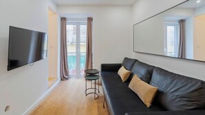 A modern living room with a black leather sofa, a flat-screen TV mounted on the wall, and a small round table. - True Setúbal, Residence (Setúbal)