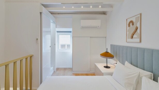 A bedroom with a bed, a nightstand, a lamp, a wall-mounted air conditioner, and a window. - True Setúbal, Residence (Setúbal)