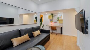 A modern living room with a black leather sofa, a flat-screen TV mounted on the wall, and a small desk with a chair. - True Setúbal, Residence (Setúbal)