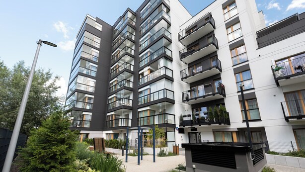 Un immeuble d’appartements moderne doté de nombreux balcons, d’une cour intérieure et entouré de verdure.