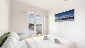 Une chambre d’hôtel avec un lit, un tableau représentant un paysage urbain et une fenêtre donnant sur des immeubles.