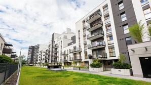 Un immeuble résidentiel moderne doté de nombreux balcons, d’une pelouse bien entretenue et surplombant un ciel dégagé.