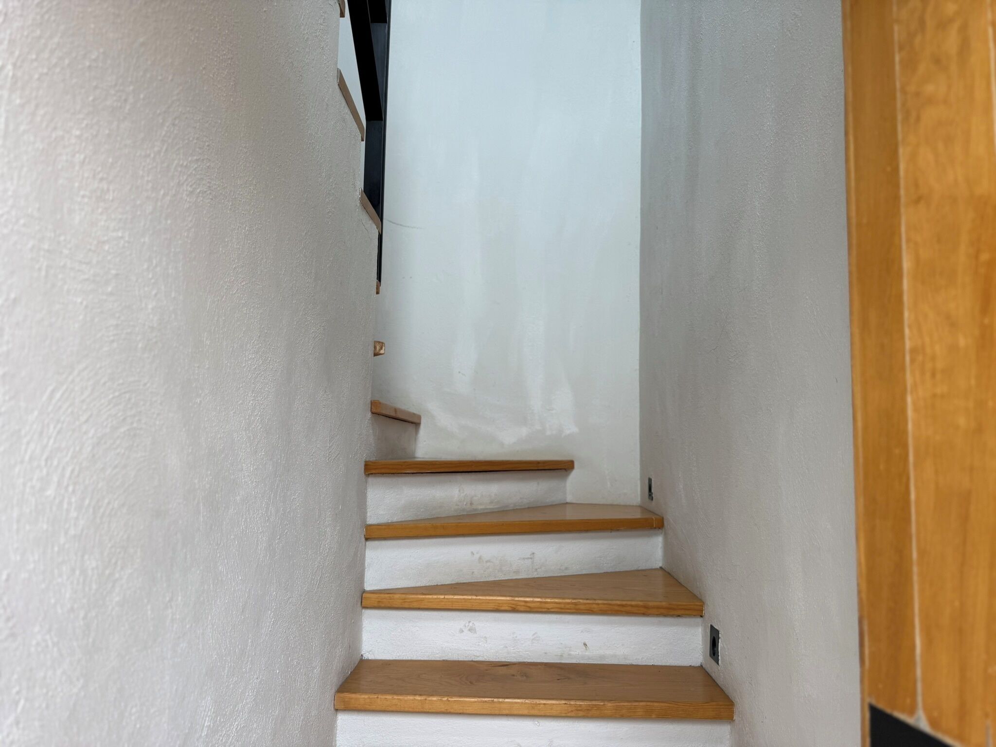 A narrow staircase with wooden steps and white walls.