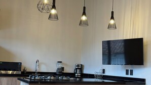 Una cuina moderna amb una illa central, tamboretes de bar, un televisor de pantalla plana i llums penjants.